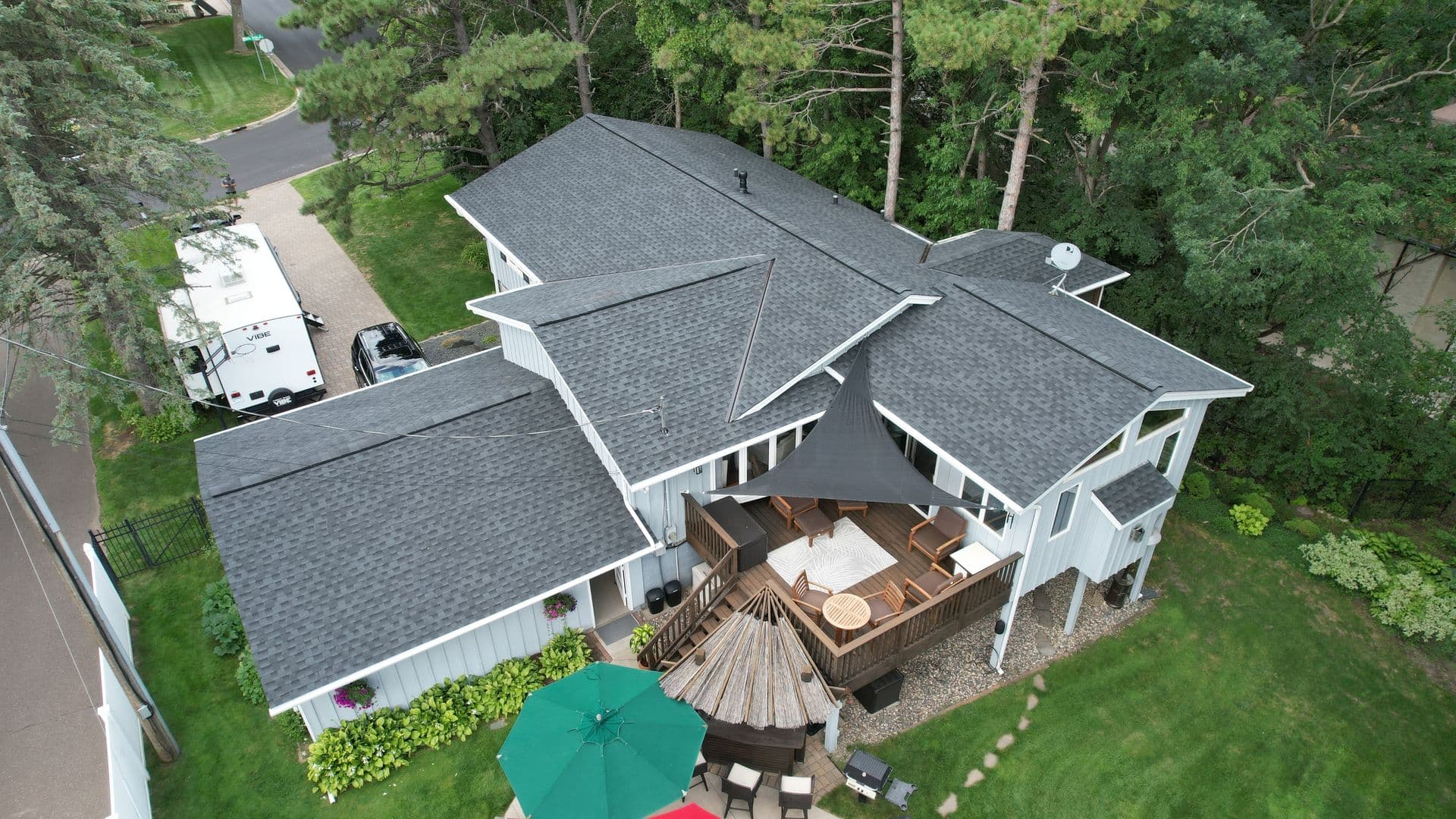 Drone view of gray asphalt shingle roof with multiple slopes and backyard deck