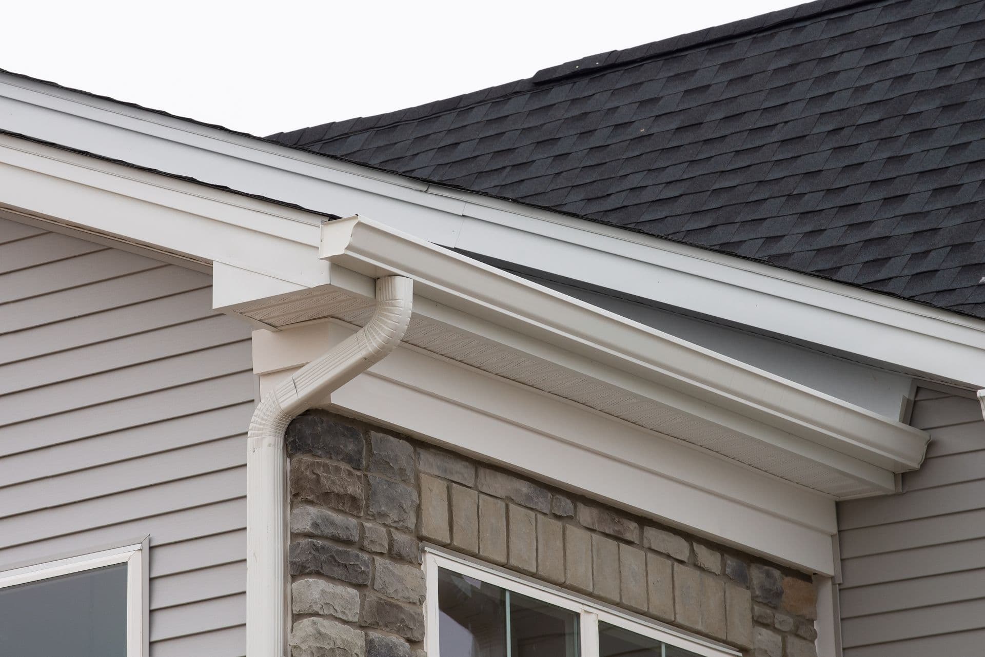 A close-up of a the corner of a house with white gutters, downspout, and soffit boards.