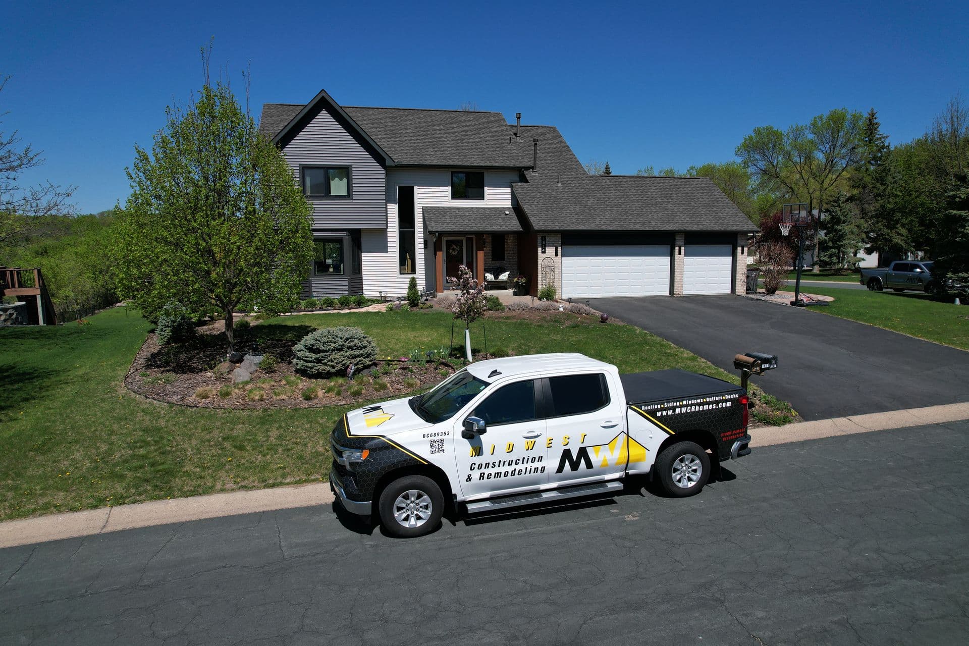 Midwest Construction & Remodeling truck parked outside a Twin Cities home with a gray asphalt shingle roof and landscaped front yard.