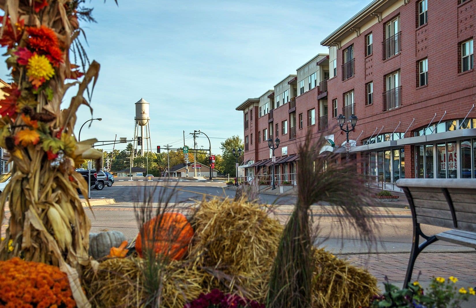Fall decorations along a downtown street in Elk River, Minnesota, with storefronts and a water tower in the background.