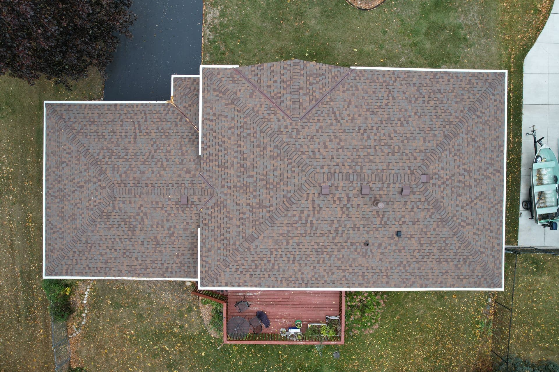 An overhead aerial view of a house with new brown shingle roofing and white gutters.