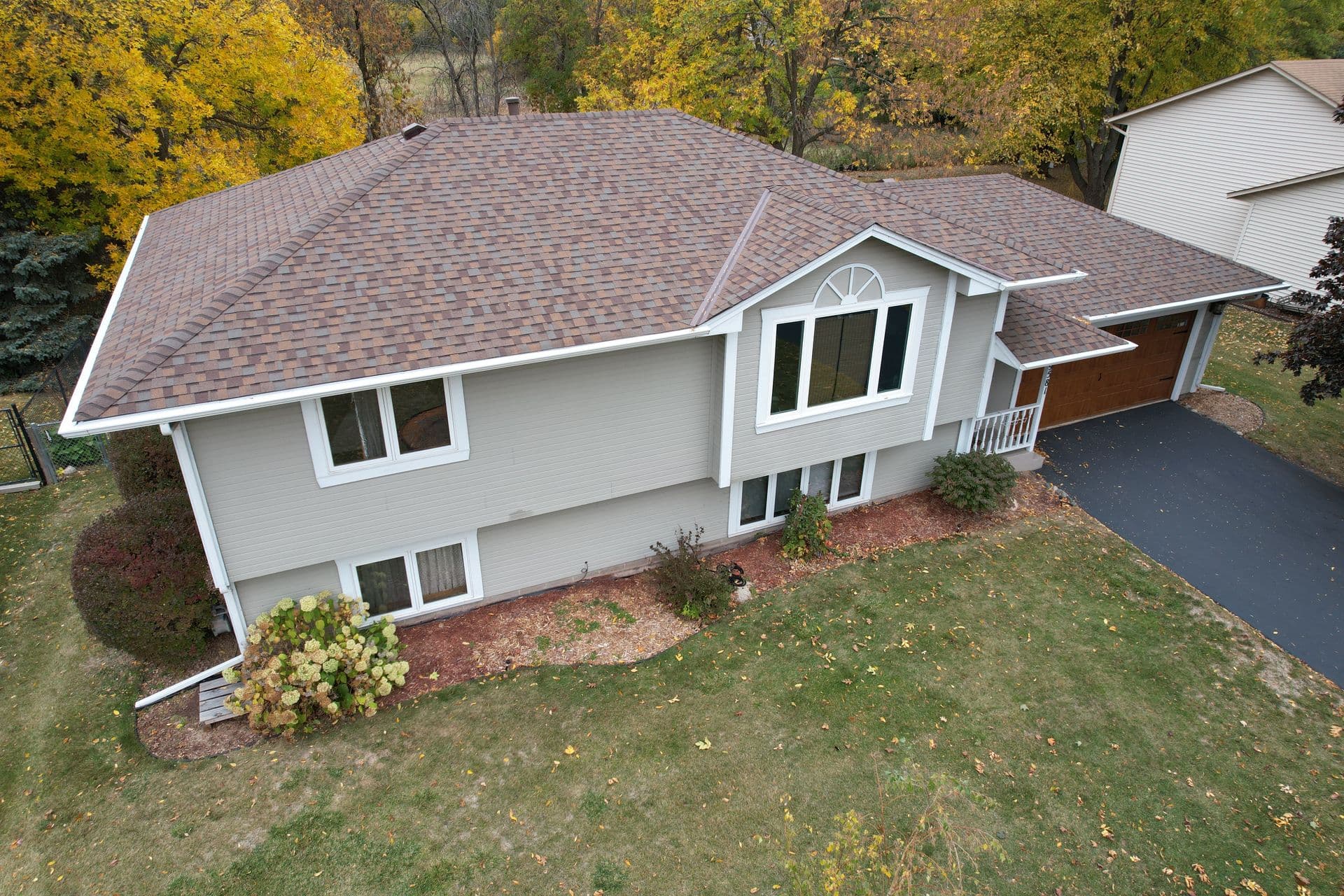 A gray house with new brown shingle roofing and white gutters.