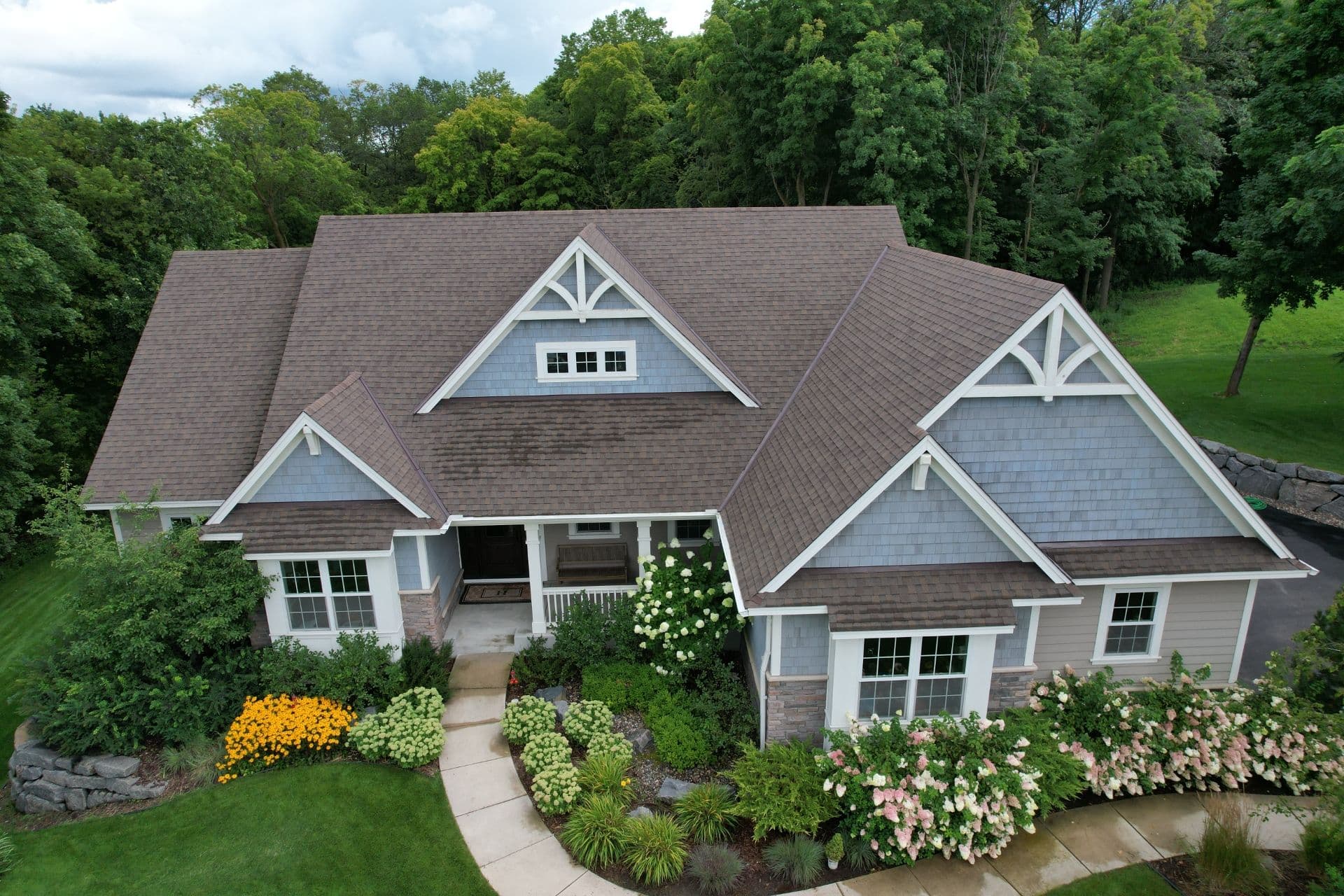 An aerial view of a house with blue shingle siding, gray shingle roofing, and stone foundation.
