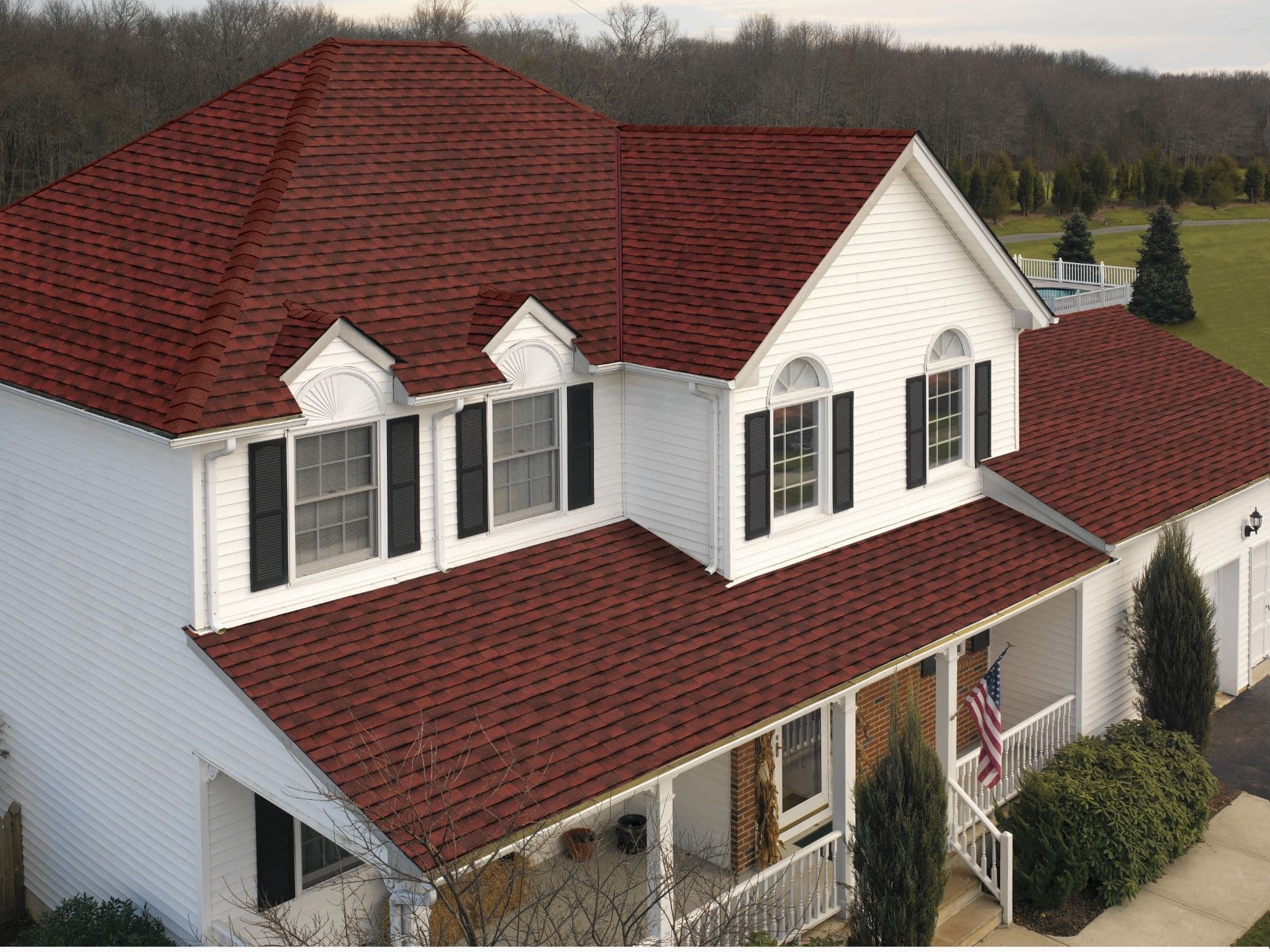 A white house with black shutters and new red shingle roofing.