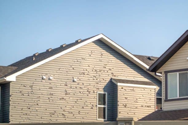 A tan house with hail-damaged siding.