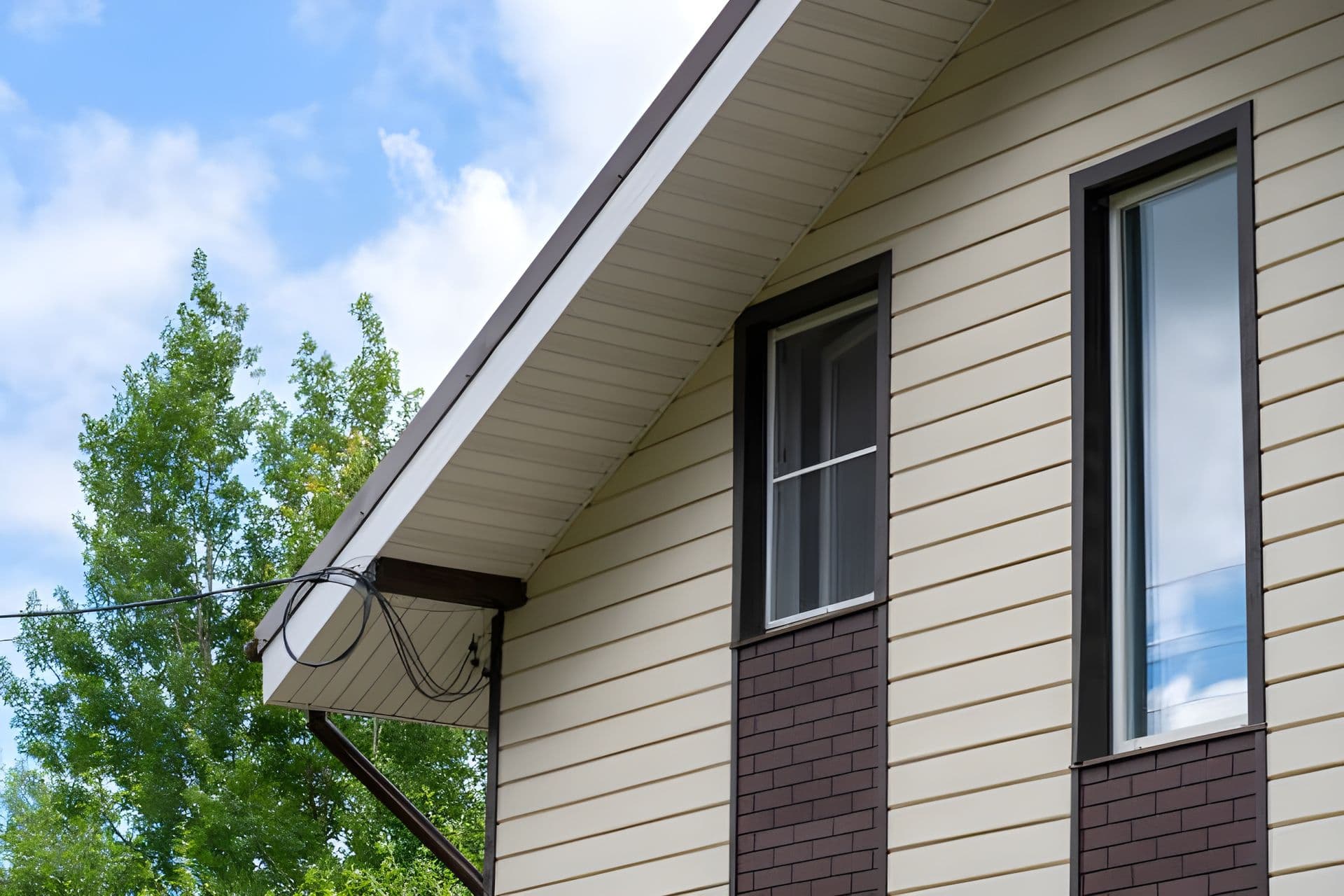 A beige house with dark brick sections and newly-replaced white soffit and fascia.