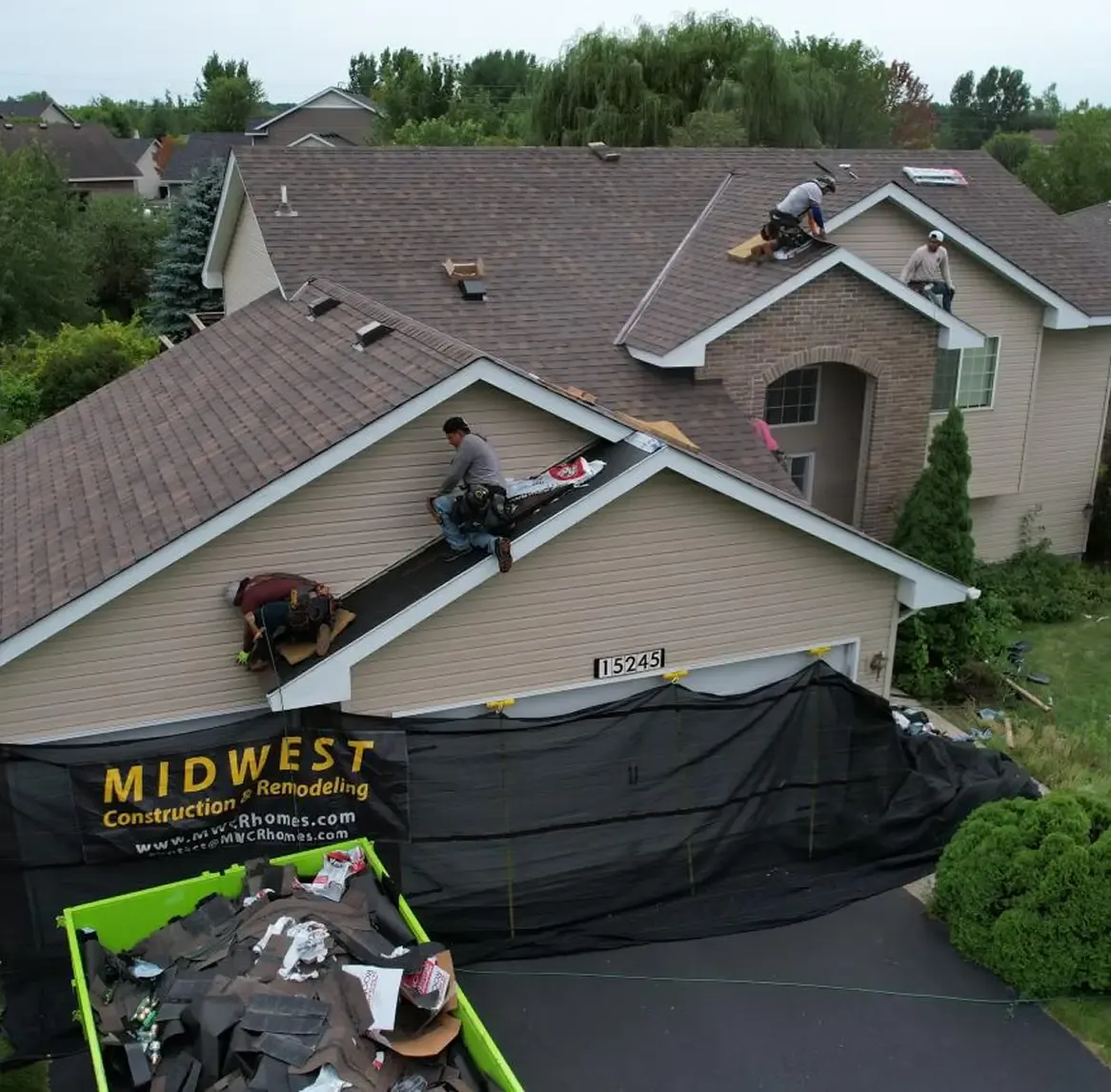 Workers install roofing on a house with a Midwest Construction & Remodeling banner out front.
